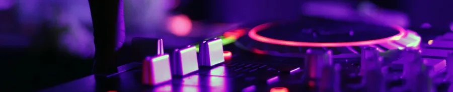 Κοντινό πλάνο σε κονσόλα DJ με φωτιζόμενα κουμπιά και jog wheel σε μωβ και κόκκινο φωτισμό.