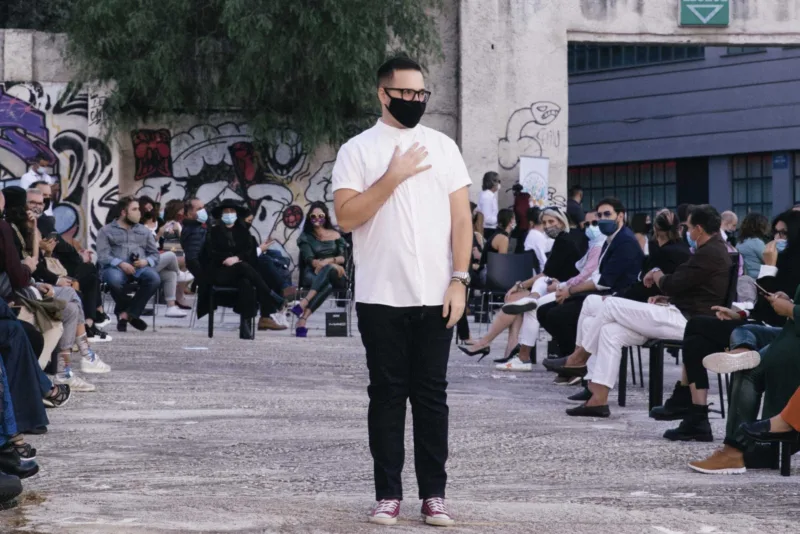 Άνδρας με λευκό πουκάμισο και μαύρη μάσκα σε υπαίθρια επίδειξη μόδας.