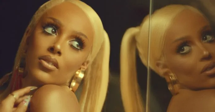 Η Doja Cat με ξανθά μαλλιά και χρυσούς κρίκους μπροστά από καθρέφτη.