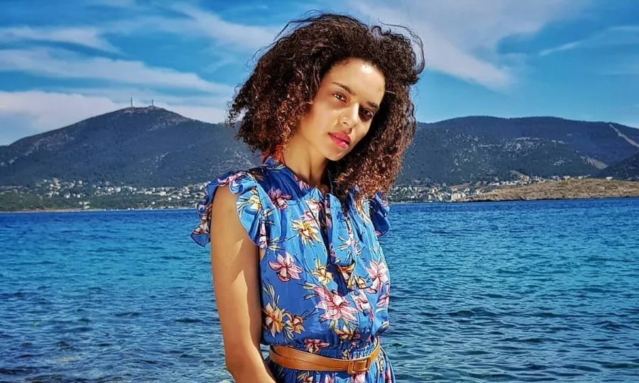 Η Μαριάννα Παινέση ποζάρει με φόντο τη θάλασσα και βουνά.