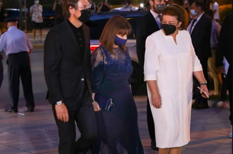 Άνδρας και δύο γυναίκες με επίσημα ενδύματα και μάσκες προστασίας σε εκδήλωση.