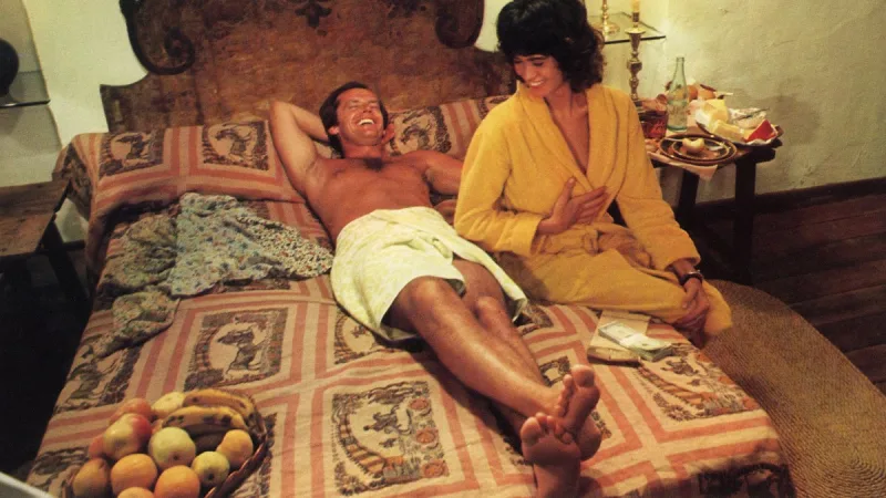 Ο Jack Nicholson ξαπλωμένος σε κρεβάτι δίπλα σε γυναίκα με κίτρινη ρόμπα.