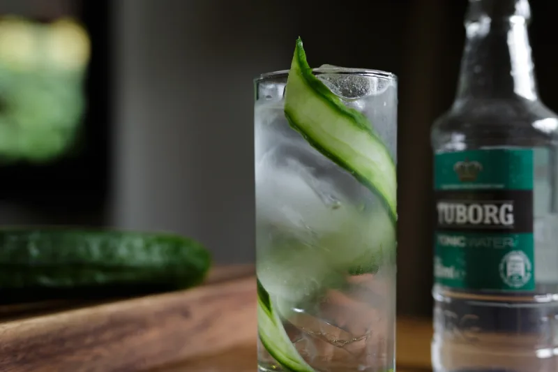 Ποτήρι με Gin Tonic, πάγο και φέτες αγγουριού δίπλα σε μπουκάλι Tuborg Tonic Water.