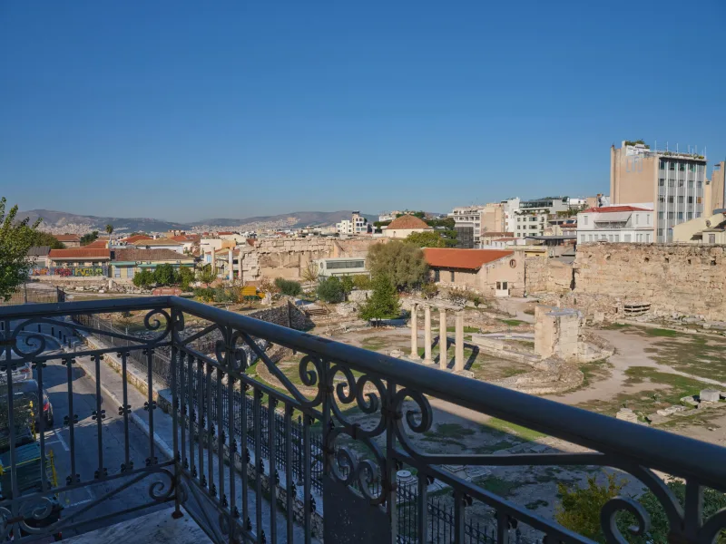 Θέα από μπαλκόνι σε αρχαιολογικό χώρο στην Αθήνα με κτίρια στο βάθος.