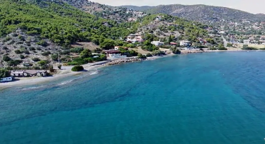 Πανοραμική άποψη της παραλίας Περιστέρια στη Σαλαμίνα με καταγάλανα νερά και καταπράσινο λόφο.