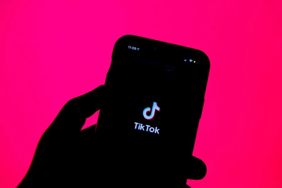 Κοντινό πλάνο χεριού που κρατάει smartphone με το λογότυπο του TikTok σε ροζ φόντο.