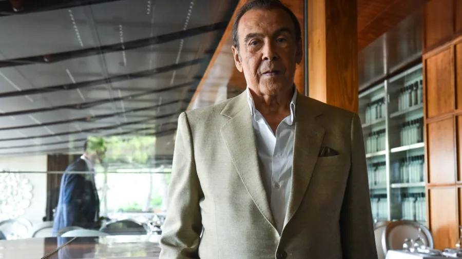 Ο Τόλης Βοσκόπουλος με μπεζ σακάκι και λευκό πουκάμισο.