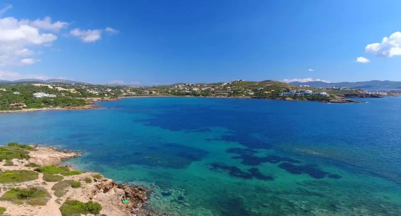 Πανοραμική άποψη παραλίας στην Αττική με γαλαζοπράσινα νερά και βραχώδη ακτογραμμή.