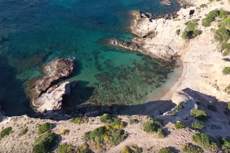 Πανοραμική άποψη μιας μικρής, απόκρημνης παραλίας με κρυστάλλινα γαλαζοπράσινα νερά και βράχια.