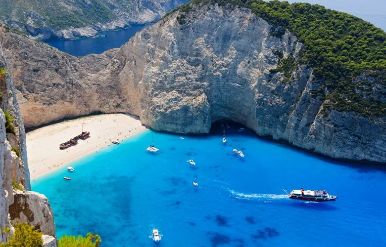 Πανοραμική άποψη της παραλίας Ναυάγιο στη Ζάκυνθο με γαλάζια νερά και πλοία.