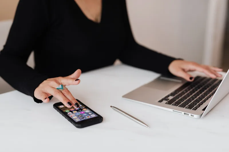 Γυναίκα που χρησιμοποιεί smartphone και laptop σε λευκό γραφείο.