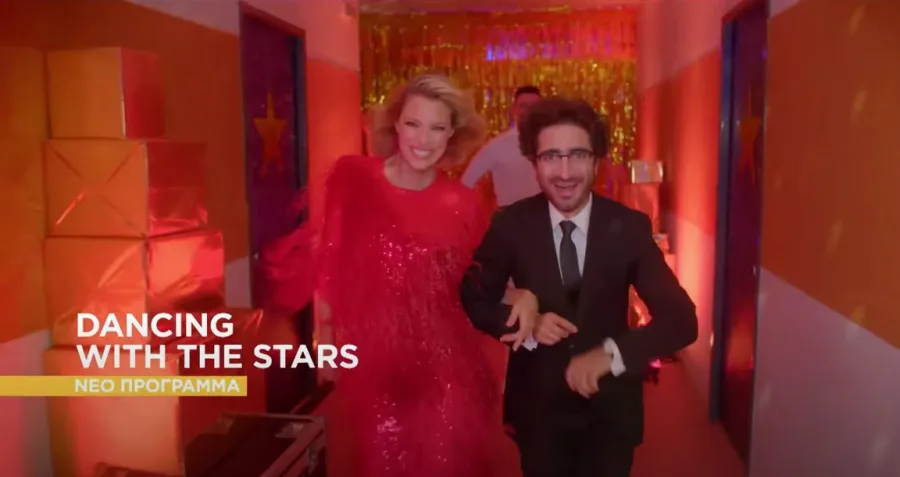 Παρουσιαστές του Dancing with the Stars σε διάδρομο με γιορτινή διακόσμηση.