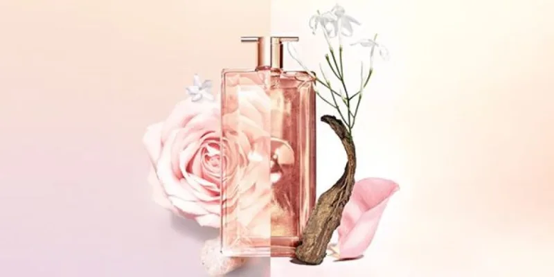 Μπουκάλι αρώματος Lancôme Idôle Aura ανάμεσα σε τριαντάφυλλο και γιασεμί.