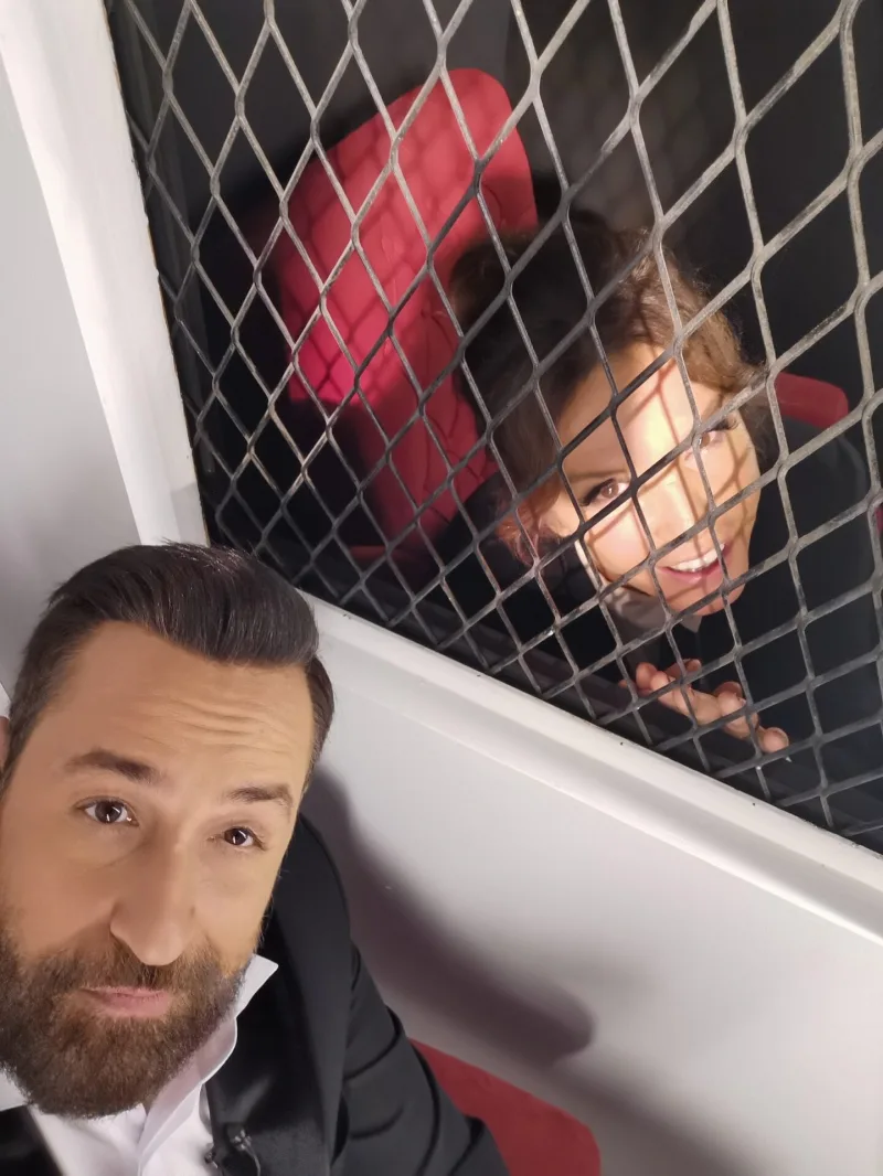 Ο Θέμης Γεωργαντάς σε selfie με γυναίκα πίσω από μεταλλικό πλέγμα.