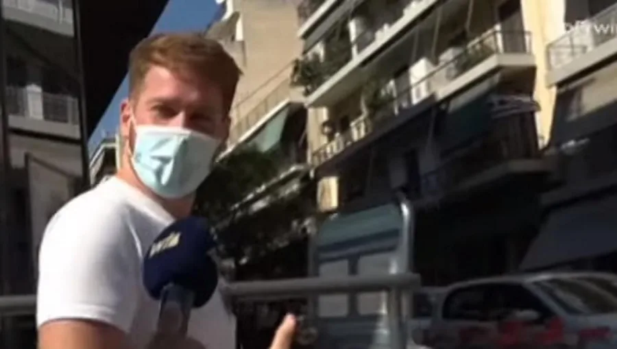 Ο James Καφετζής με προστατευτική μάσκα και μικρόφωνο σε εξωτερικό χώρο.