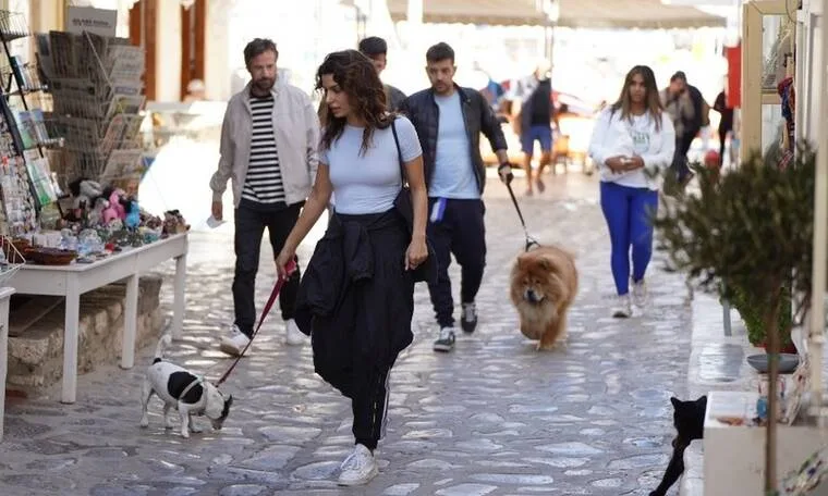Η Τόνια Σωτηροπούλου και ο Κωστής Μαραβέγιας περπατούν σε πλακόστρωτο δρομάκι στην Ύδρα με τα σκυλιά τους.