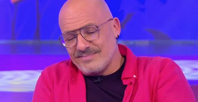 Ο Νίκος Μουτσινάς με γυαλιά και κόκκινο πουκάμισο σε τηλεοπτικό πλατό.