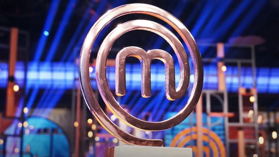 Το χάλκινο λογότυπο του MasterChef σε στούντιο με μπλε φωτισμό.