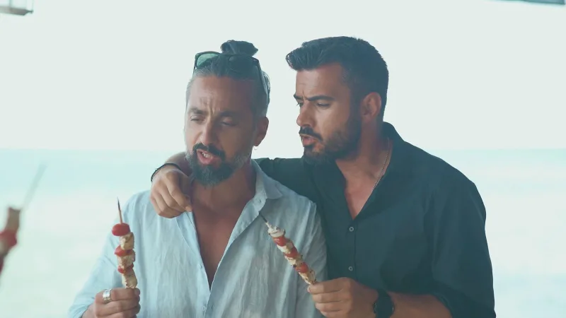 Ο Γιάννης Τσιμιτσέλης και ο Αναστάσης Κολοβός κρατούν σουβλάκια ψαριού.