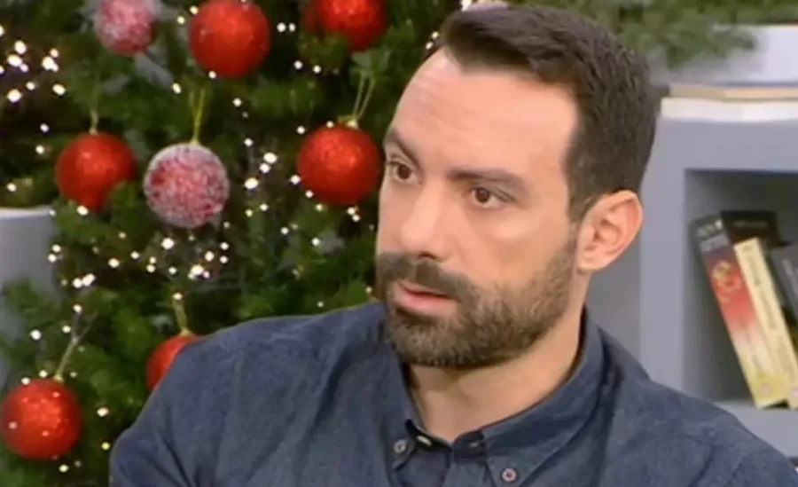 Ο Σάκης Τανιμανίδης σε τηλεοπτική εμφάνιση με φόντο χριστουγεννιάτικο δέντρο.