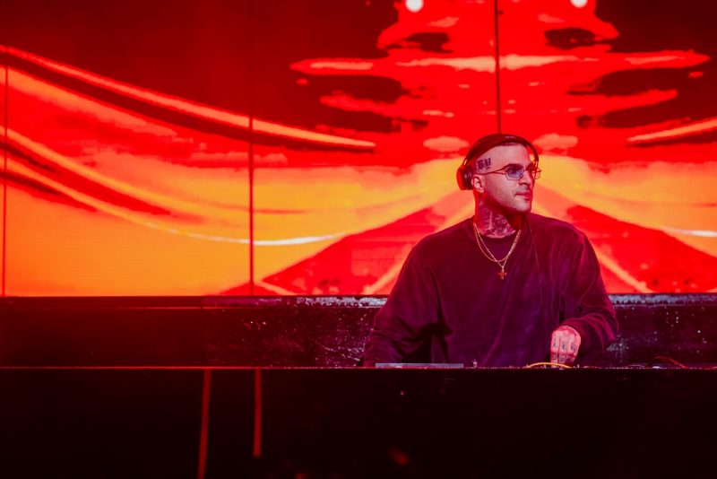 DJ με τατουάζ και ακουστικά σε σκηνή με κόκκινο φόντο