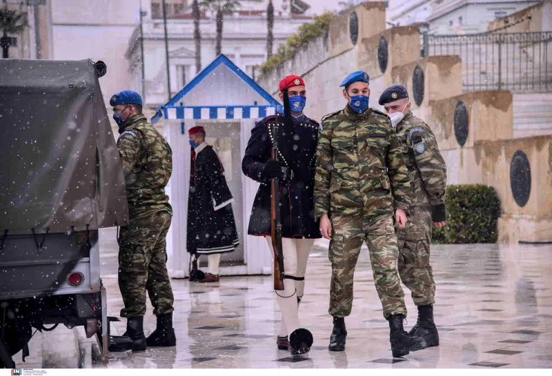 Εύζωνας με χειμερινή στολή και στρατιώτες με παραλλαγή και μάσκες στο Σύνταγμα.