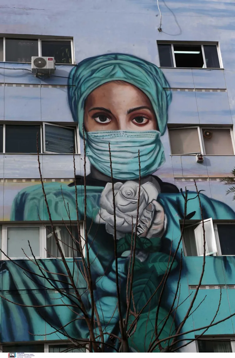 Graffiti νοσηλεύτριας με μάσκα και λευκό τριαντάφυλλο σε τοίχο νοσοκομείου.