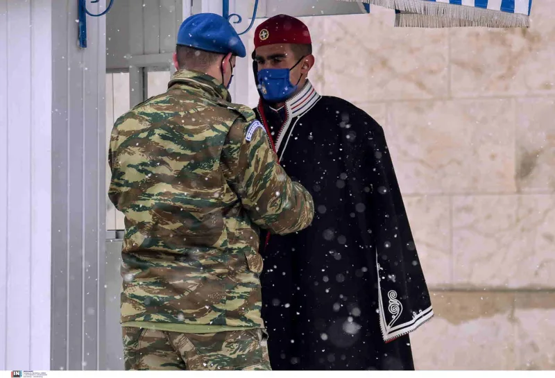 Ένας στρατιώτης βοηθά έναν Εύζωνα με τη χειμερινή του ενδυμασία κατά τη διάρκεια χιονόπτωσης.