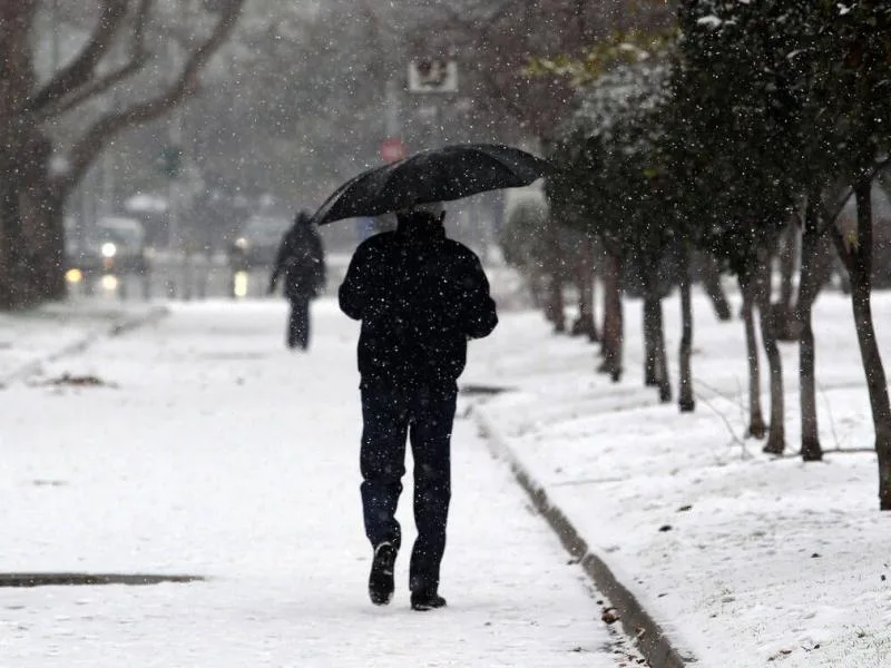 Άνθρωπος με ομπρέλα περπατά σε χιονισμένο δρόμο