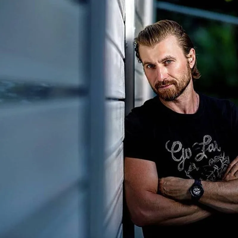 Γνωστός ηθοποιός με μούσια και μαύρο t-shirt ακουμπισμένος σε τοίχο.