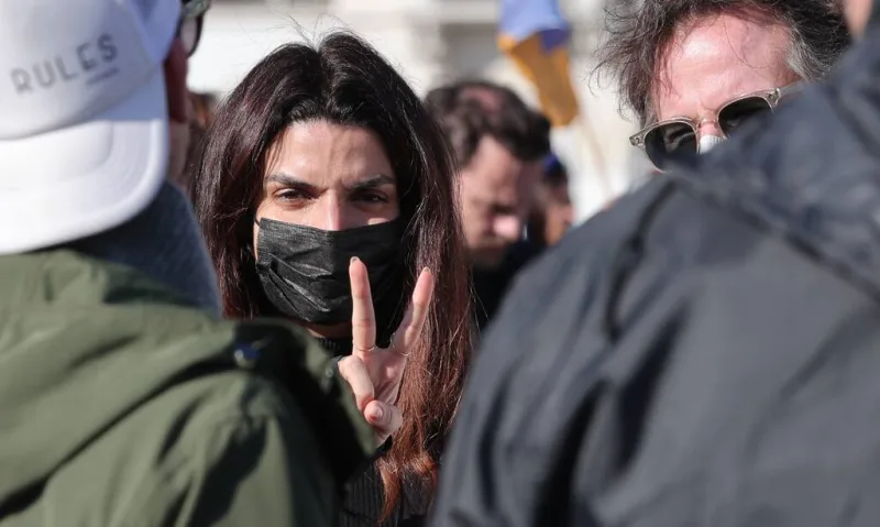 Γυναίκα με μαύρη μάσκα προστασίας κάνει το σήμα της ειρήνης σε αντιπολεμική συγκέντρωση.