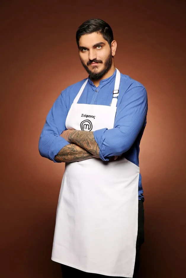 Ο Στέφανος, ένας από τους 24 παίκτες του MasterChef, ποζάρει με ποδιά και σταυρωμένα χέρια στο σπίτι του ριάλιτι.