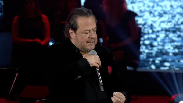 Ο Γιάννης Πάριος τραγουδάει με μικρόφωνο στη σκηνή.