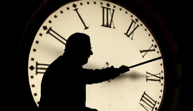 Σιλουέτα άνδρα μπροστά από ένα μεγάλο φωτιζόμενο ρολόι με λατινικούς αριθμούς.