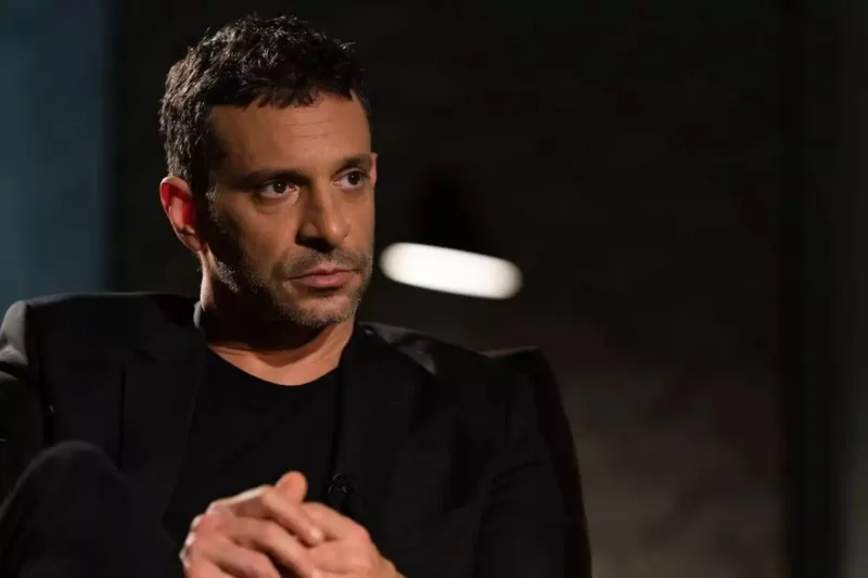 Έλληνας καλλιτέχνης με μαύρο σακάκι και μπλούζα σε σκοτεινό φόντο