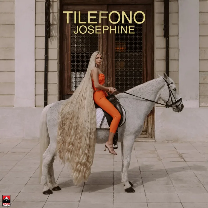 Η Josephine με πορτοκαλί σύνολο και πολύ μακριά μαλλιά πάνω σε λευκό άλογο.