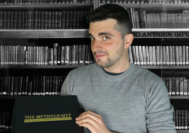 Ο The Mythologist κρατάει ένα μαύρο κουτί με το λογότυπό του μπροστά από μια βιβλιοθήκη.