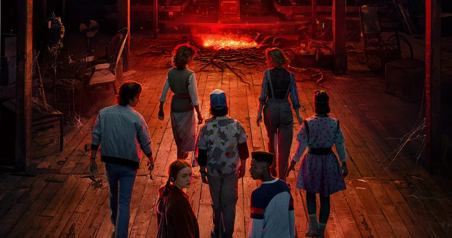 Πρωταγωνιστές της σειράς Stranger Things σε σκοτεινό ξύλινο χώρο με κόκκινο φως.
