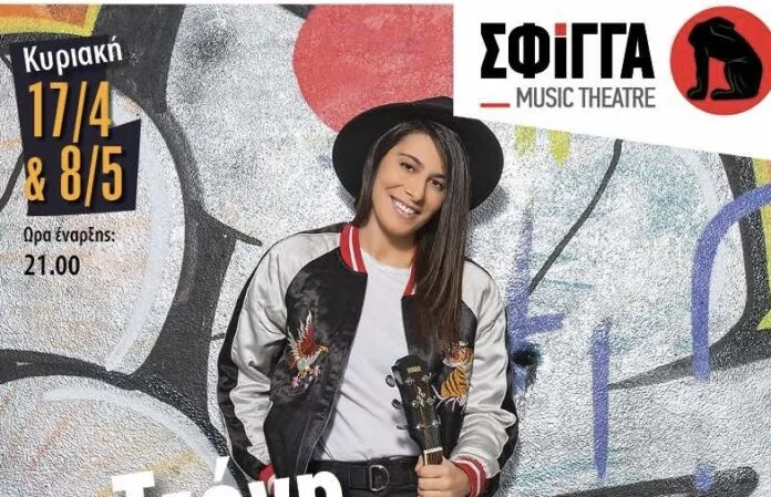 Η Τζένη Γεωργιάδη με καπέλο και bomber jacket κρατώντας κιθάρα μπροστά από τοίχο με γκράφιτι.
