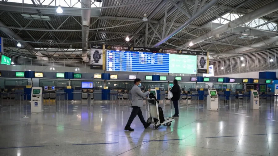 Άποψη άδειου αεροδρομίου με επιβάτες που φορούν μάσκες.