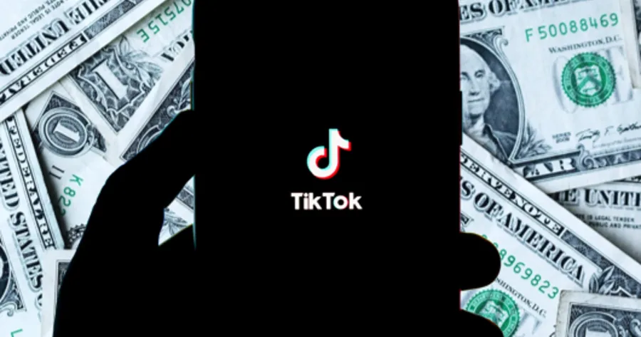 Το λογότυπο του TikTok σε οθόνη κινητού πάνω από χαρτονομίσματα δολαρίων.