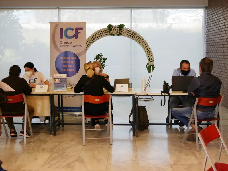 Άνθρωποι σε γραφεία ενημέρωσης με banner του ICF Greece.