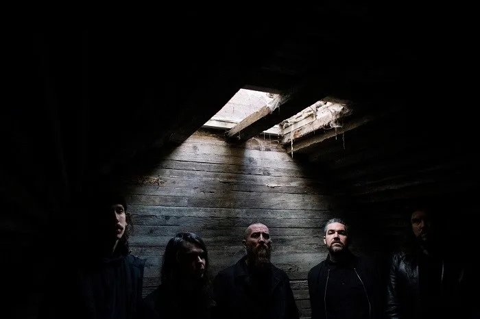 Πέντε μέλη ενός metal συγκροτήματος σε σκοτεινό ξύλινο χώρο.