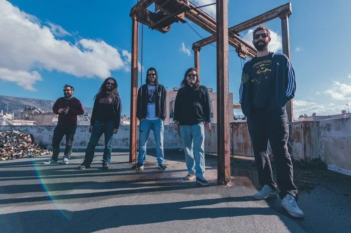 Πενταμελές rock συγκρότημα σε ταράτσα με βιομηχανικό εξοπλισμό.