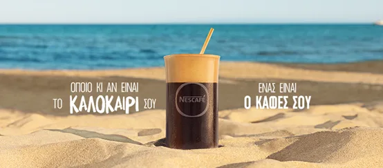 Ένα ποτήρι Nescafé Frappé στην άμμο με φόντο τη θάλασσα.