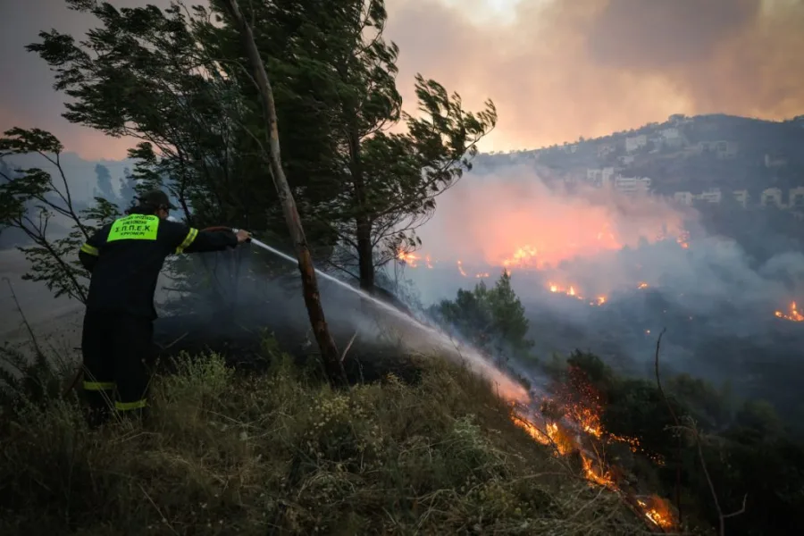 Πυροσβέστης επιχειρεί με μάνικα σε δασική πυρκαγιά.
