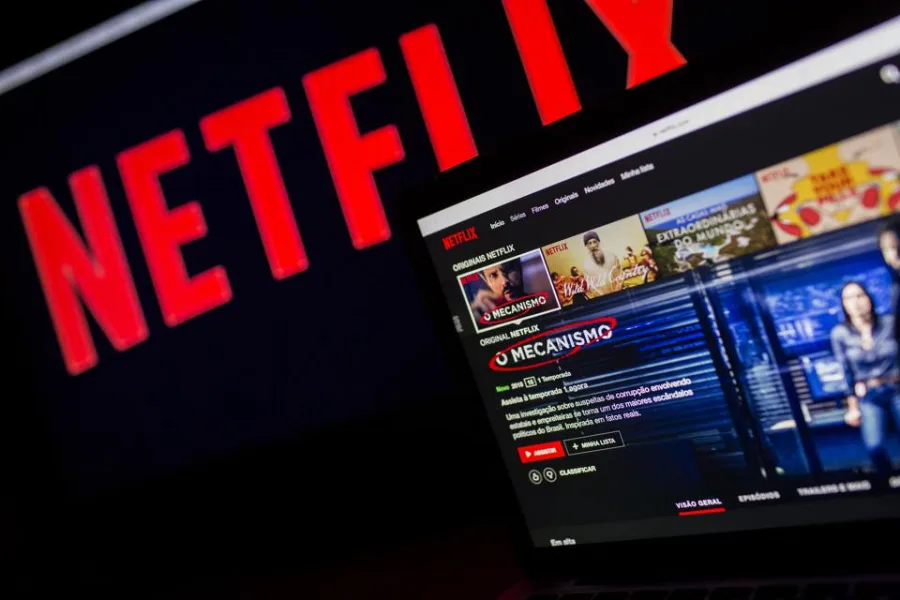 Το λογότυπο του Netflix σε οθόνη και ένας φορητός υπολογιστής που δείχνει την πλατφόρμα.