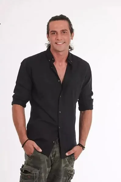 Άνδρας παίκτης του Love Island με μαύρο πουκάμισο και παντελόνι παραλλαγής.