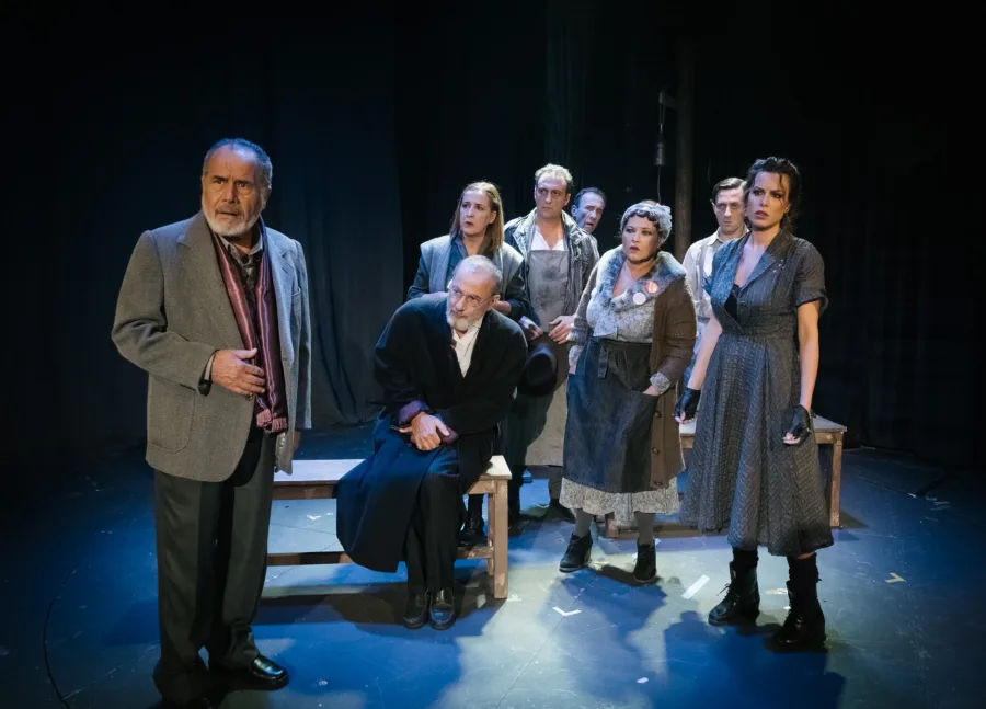 Σκηνή από τη θεατρική παράσταση Dogville με ομάδα ηθοποιών στη σκηνή.