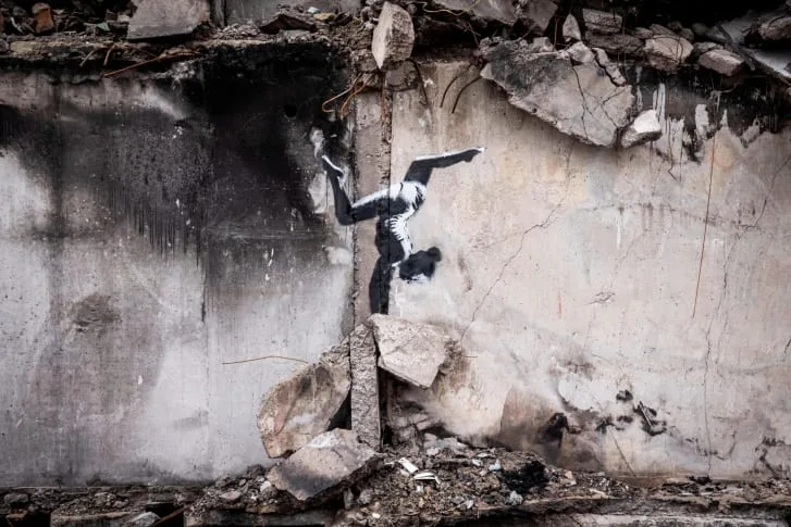 Graffiti του Banksy στην Ουκρανία που απεικονίζει μια γυμνάστρια να κάνει κατακόρυφο πάνω σε ερείπια.